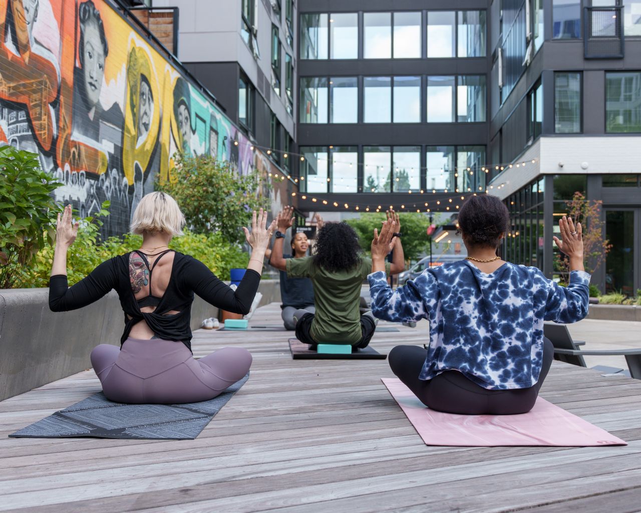 A diverse group of adults practicing yoga outdoors in a vibrant urban setting.