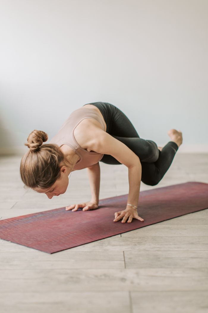 about-us-01 Woman performing crow pose on yoga mat indoors for strength and balance.